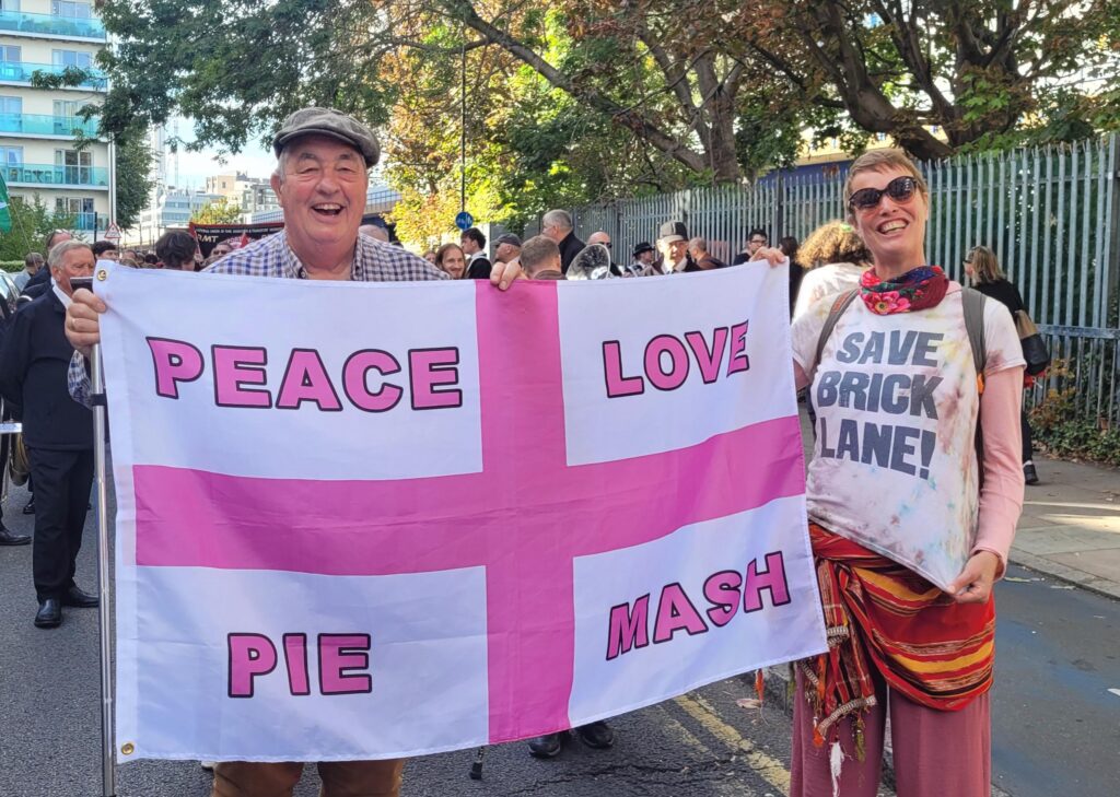 Andy Green of Grow Social Capital at the 90th anniversary of the Battle Cable of Street, proudly showing his adapted St George Cross saying 'Peace, Love, Pie and Mash', with a pink cross replacing the red